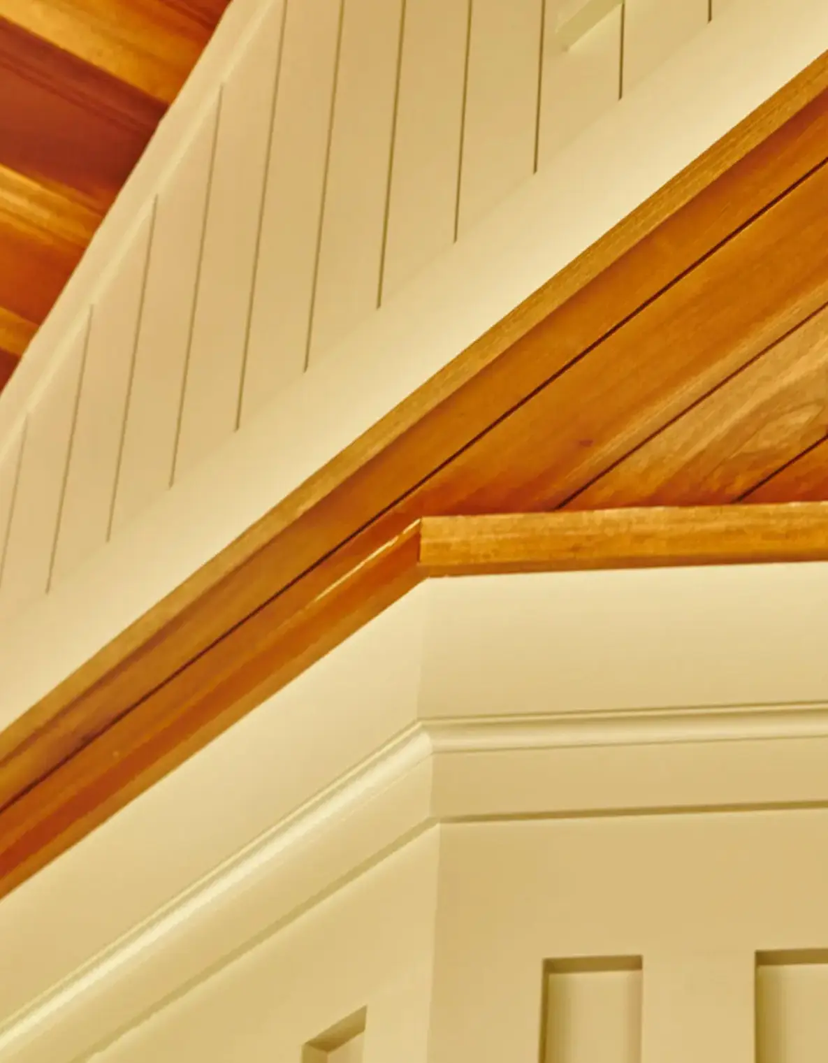 Close-up of wooden and white paneled ceiling corner with warm lighting.