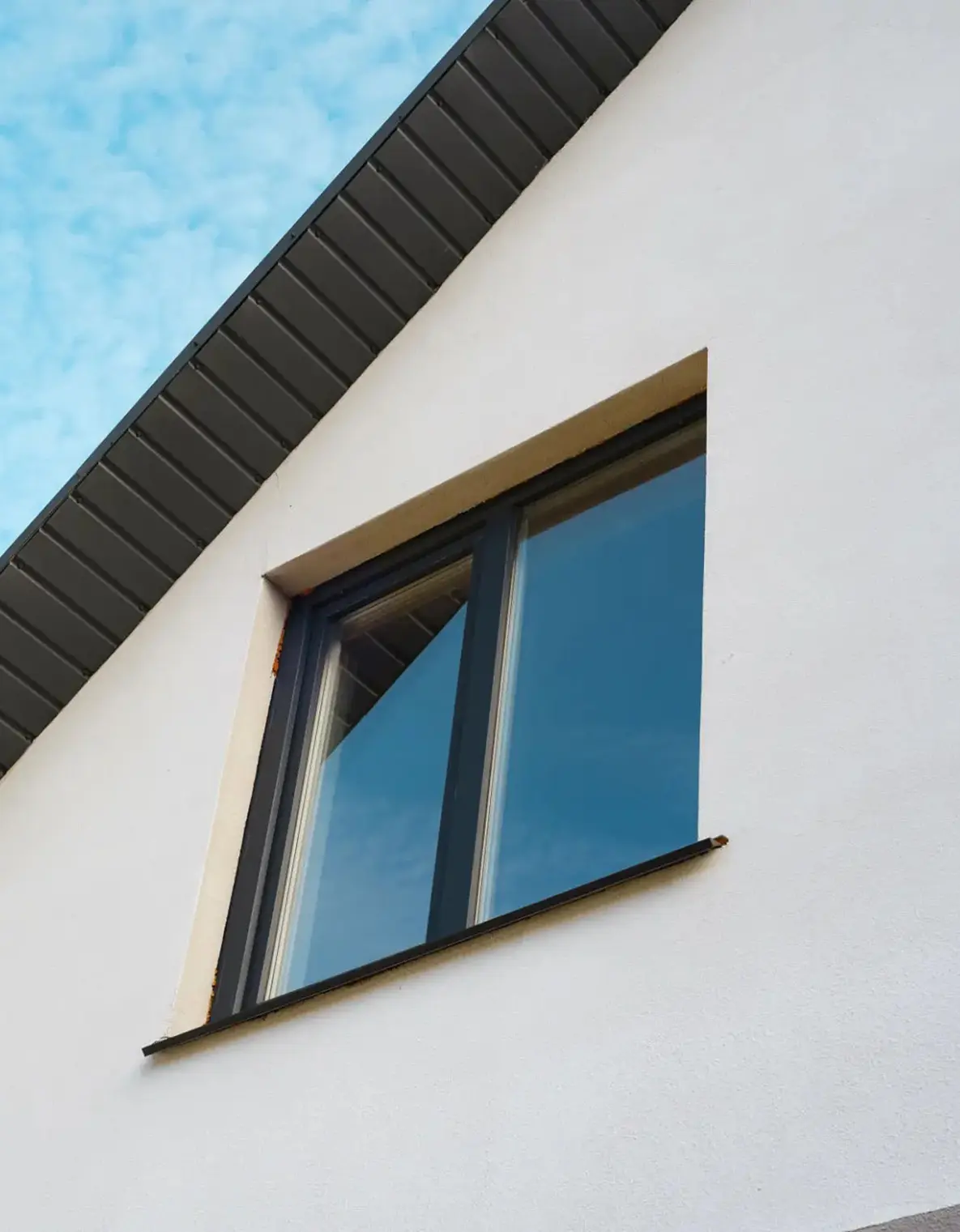 Modern window reflecting the sky on a white building.