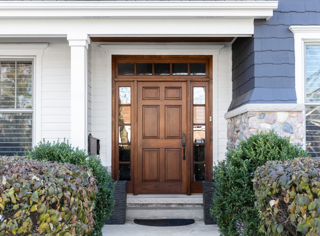 Elegant wooden front door framed by white pillars and greenery.